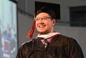 Male graduate student walking and smiling